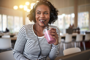 Smiling young African college student drinking a smoothie betwee