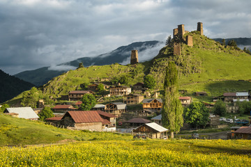 Scenic landscape of early summer morning in the depths of the Caucasus mountains. Sun just came out and illuminates ancient ruins of tushetian towers. Below the ruins is the village Upper Omalo.