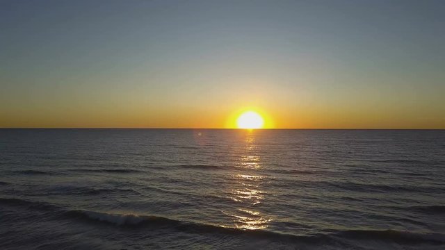 A golden sun slowly sets over the ocean, aerial