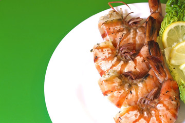 Ready cooked, fried, prepared tiger prawns with lettuce and lemon slices in a plate. Sea shrimp. Top view. Green background.
