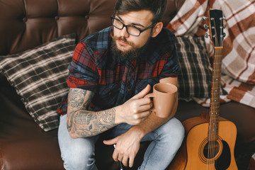 Young guitarist hipster at home with guitar rest drinking tea