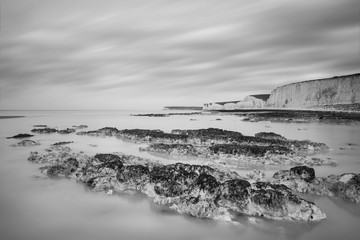 Stunning black and white long exposure landscape image of low tide beach with rocks at sunrise