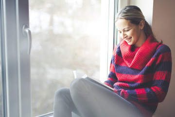 young beautiful woman is reading book an windowsill