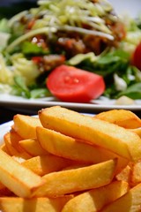 Crispy chunky chips with mixed salad topped with roast vegetables to the rear on a wooden table,...