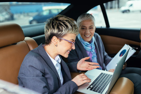 Senior business woman and her assistant sitting in limousine talking and working