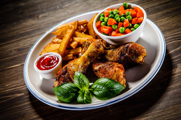 Grilled chicken legs with French fries and vegetables on wooden table background