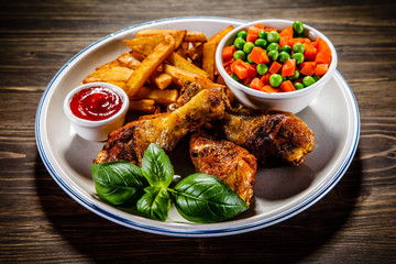 Grilled chicken legs with French fries and vegetables on wooden table background