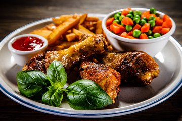 Grilled chicken legs with French fries and vegetables on wooden table background