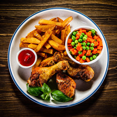Grilled chicken legs with French fries and vegetables on wooden table background