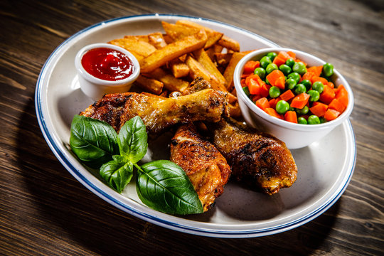 Grilled chicken legs with French fries and vegetables on wooden table background