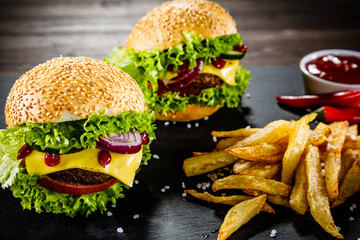 Two tasty cheeseburgers with french fries served on fashionable black desk