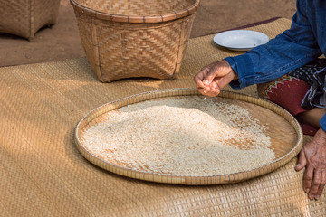 Farmer asian woman picking up and select good rice grains from rice in bamboo basket.