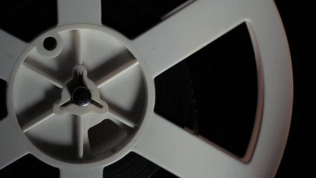 Old 8mm film projector playing in the night. Close-up of a reel with a film. Rotation reel with tape on the video, audio tape recorder or player.