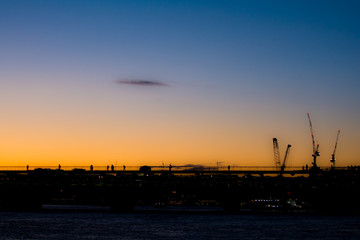 Silhoutted people crossing a city bridge at sunset