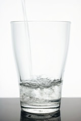 Glass beaker into which Water flows. Water is clean - glass is transparent. Glass on a white background. Water is pure ecology