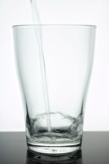 Glass beaker into which Water flows. Water is clean - glass is transparent. Glass on a white background. Water is pure ecology
