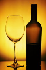 Glass and a Bottle of Wine. Bottle is open, half of it is Wine. Glass and Bottle of wine on a yellow background with a black vignette. Ellegant forms of Bottlr and Glass