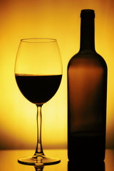 Glass and a Bottle of Wine. Bottle is open, half of it is Wine. Glass and Bottle of wine on a yellow background with a black vignette. Ellegant forms of Bottlr and Glass