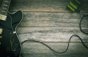 Black electric guitar, effect pedal on a rustic wooden background, green tint