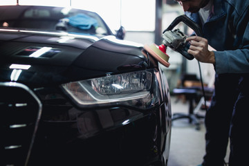 Fototapeta na wymiar Car detailing - Hands with orbital polisher in auto repair shop. Selective focus.