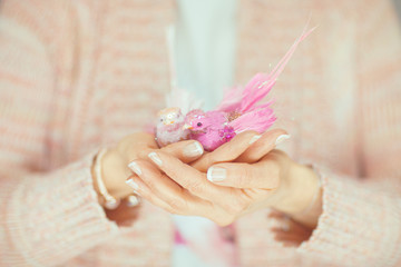 woman hands holding little artificial bird in her hands, light pink pastel colors can be used as romantic background