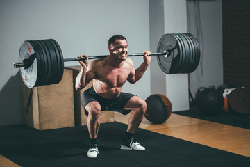 Muscular man training squats with barbells on shoulders.