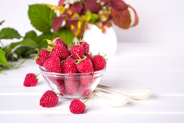 Red fresh raspberries in a glass bowl and Raspberry jam with green leaves on white background.