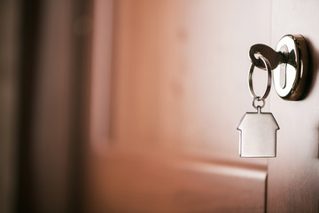 House key on a house shaped silver keyring in the lock of a entrance  brown door