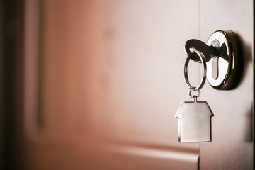 House key on a house shaped silver keyring in the lock of a entrance  brown door