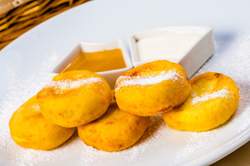Cottage cheese pancakes with honey and sour cream on white plate