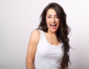 Beautiful positive excited young woman with open mouth in white shirt and long curly hair on white background with empty copy space