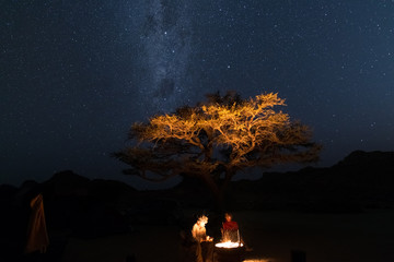 Couple at campfire, camping under starry sky and Milky Way arch. Adventure into the wild, Namibia...