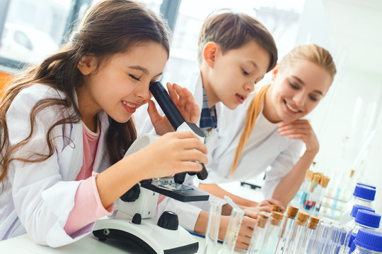 Little Kids With Teacher In School Laboratory Looking In Microscope