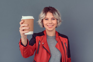 Young woman standing in leather jacket isolated on grey wall hot coffee
