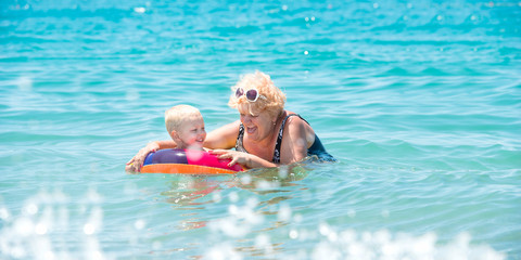  Grandmother and little grandson swim in the sea.The baby in the bouncy multicolored circle.Summer vacation.