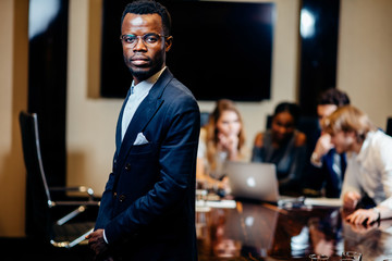 handsome african businessman looking on camera with group of businesspeople on background