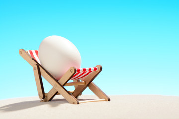 Fototapeta na wymiar Easter egg in lounger on sandy beach