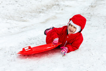 Pretty smiling little girl in her ski suit sliding down a small snow covered hill with her sledge