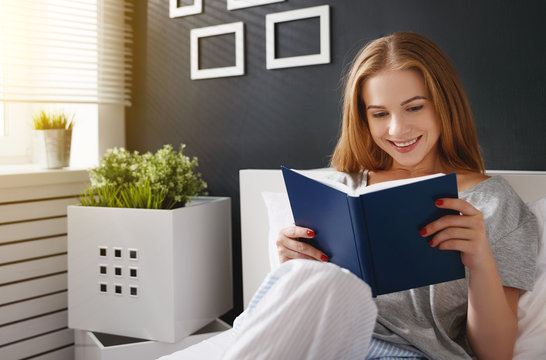 Happy young woman reads  book and drinks coffee in bed