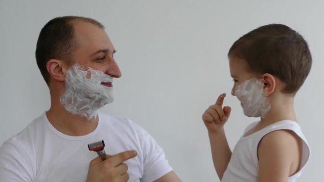 Father and son play together. Dad and little son are shaving. The boy is shaving with foam. Happy family