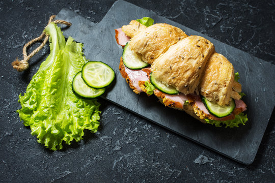 Croissant with cheese, ham, cucumber and salad on a stone background
