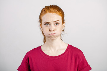 redhead woman with freckles blowing her cheeks, frowning, feeling frustrated with something