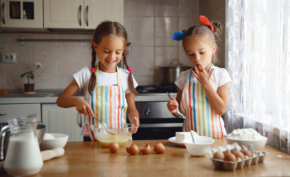 happy sisters children girls bake cookies, knead dough, play with flour and laugh