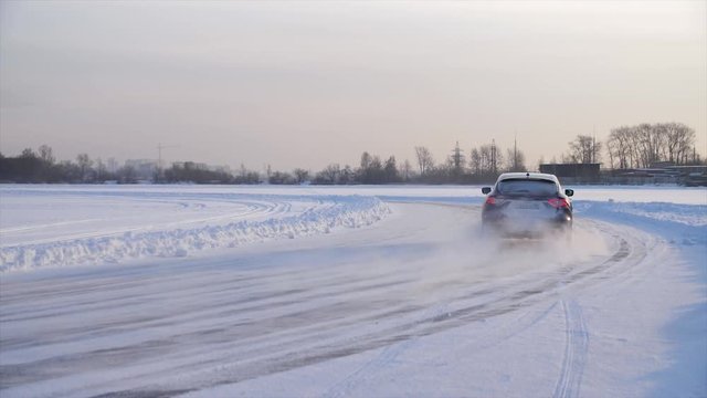Car with winter tyres installed on light alloy wheels in snowy outdoors road. A car driving down a snowy road during winter. Car drives on a snowy road