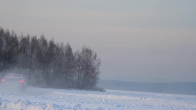 Car with winter tyres installed on light alloy wheels in snowy outdoors road. A car driving down a snowy road during winter. Car drives on a snowy road