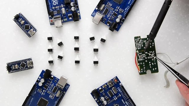 The master makes the soldering of wires against the background of the electronic boards laid out on a white table. You can see the smoke coming from rosin