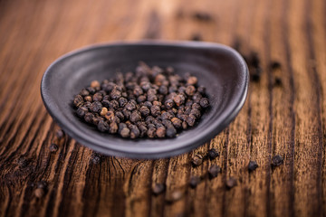 detail close up of whole black peppercorn in a black dish bowl  on wooden table
