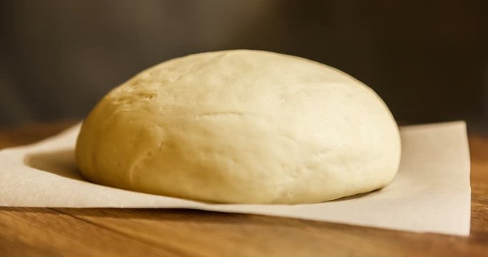 time laps. the dough rise . yeast dough rising on parchment on wooden table, on dark background. stages of cooking pizza. pizza dough