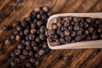 detail close up of whole black peppercorn seasoning spice in wooden spoon on wood table 