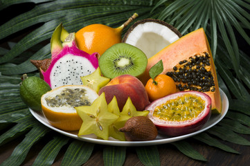 Exotic tropical fruits dish on palm leaves and wooden background, healthy food, diet nutrition,...